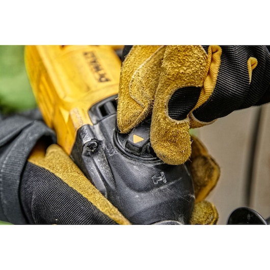 Close-up of a gloved hand adjusting a setting on a DEWALT power tool.
