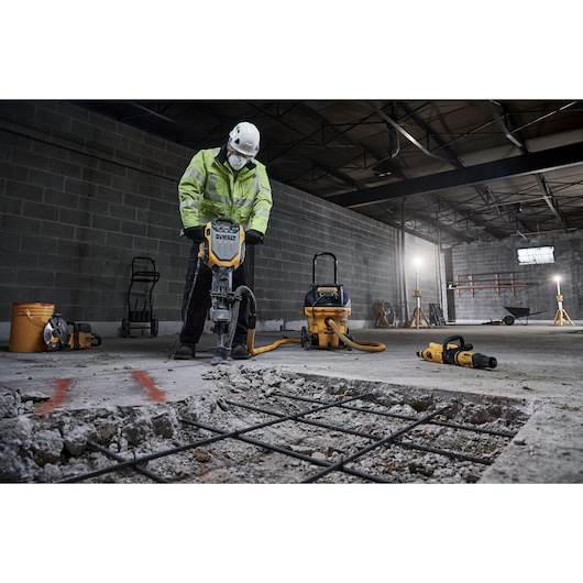 Worker uses DEWALT D25966, D25966-B2 breaker on concrete in warehouse. Construction tools are visible.