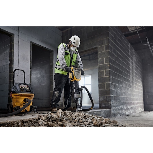 Worker uses DEWALT D25966, D25966-B2 breaking tool on debris. Construction site background.