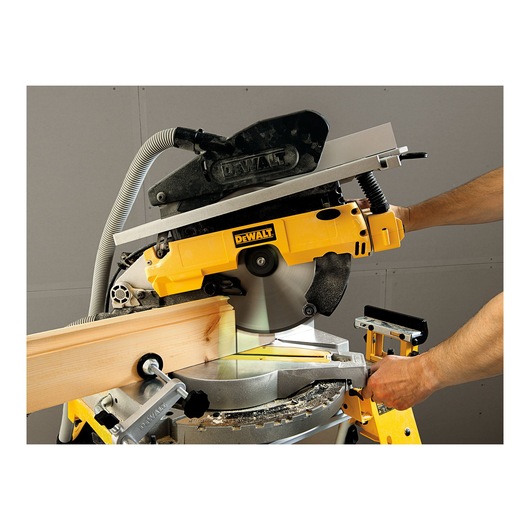 A DEWALT compound mitre saw cutting a piece of wood, operated by a person. The saw features a circular blade and a dust extraction system.