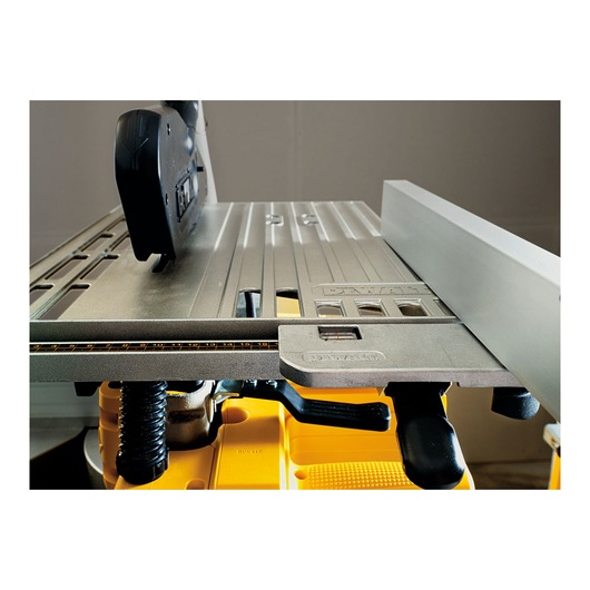 Close-up view of a DEWALT table saw, showing the metal surface with a measurement guide, adjustment levers, and fence for precise cutting.