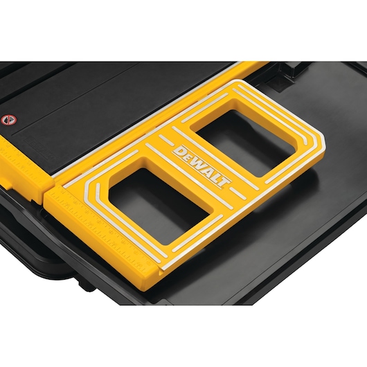 Close-up view of a DEWALT yellow measuring guide on a black surface. The guide features two rectangular openings and white accent lines, with the DEWALT logo prominently displayed in the center.