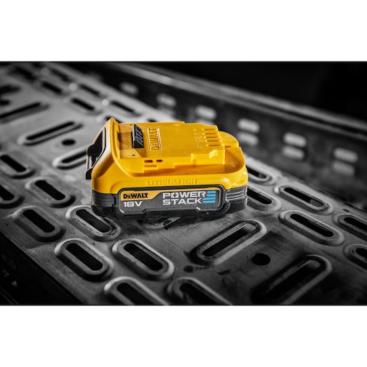 DEWALT 18V POWERSTACK lithium-ion battery resting on a textured metal surface.