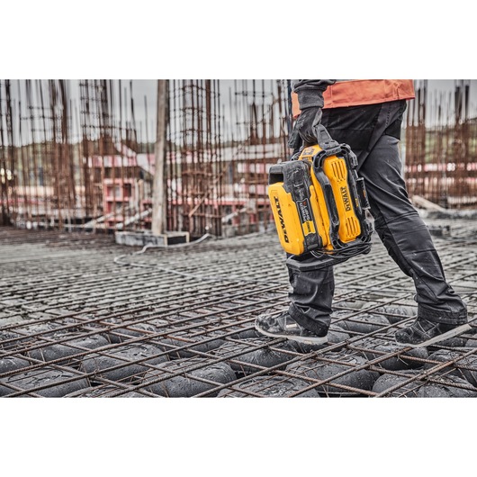 Person carrying a yellow DEWALT battery tool at a construction site with steel reinforcement and unfinished structures.