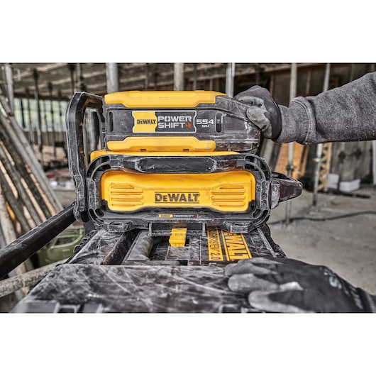 DEWALT Power Shift battery pack in use at a construction site, handled by a worker wearing gloves.