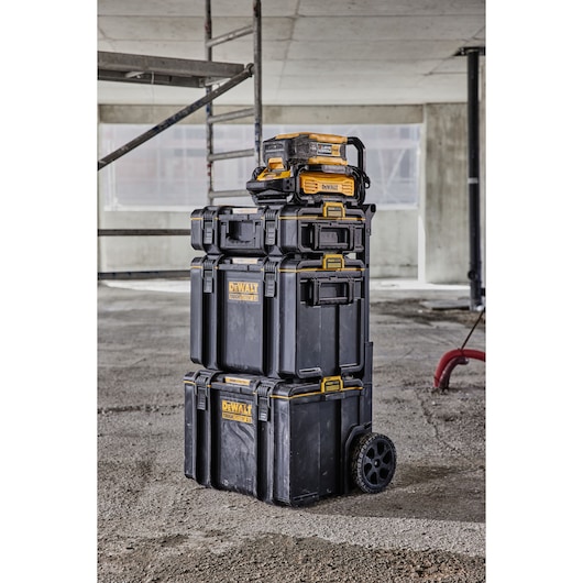 Stack of DEWALT ToughSystem tool storage boxes with wheels, shown in an industrial or construction setting.