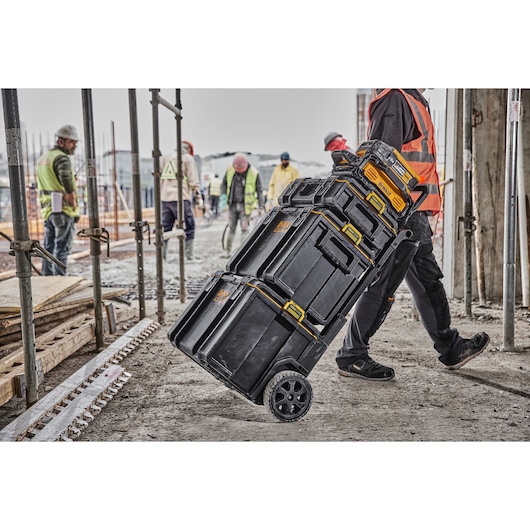 DEWALT tool storage boxes stacked on wheels, being moved at a construction site with workers in the background.