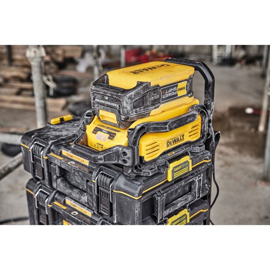 A yellow and black DEWALT battery charger and storage system, with dust marks, stacked on top of ToughSystem toolboxes at a construction site.