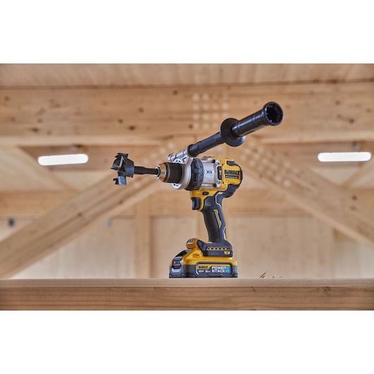 Yellow DEWALT cordless drill with handle and drill bit, placed on a wooden beam in a workshop setting.
