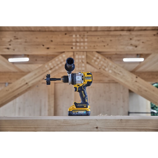A DEWALT cordless drill with battery stands on wood, set in a workshop with wooden beams in the background.