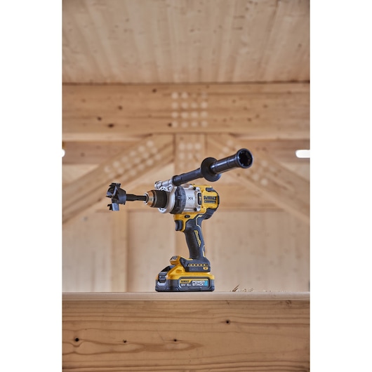 DEWALT cordless drill with Powerstack battery and side handle resting on wooden beam indoors.