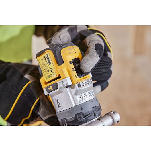 Gloved hand adjusting DEWALT cordless drill DCD1007WW1T on jobsite. Close-up of tool's control and labels.