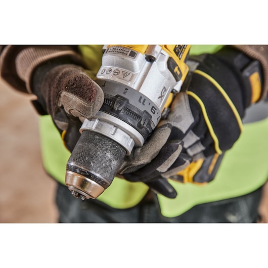 Close-up of a gloved person holding a DEWALT cordless drill in a work environment.