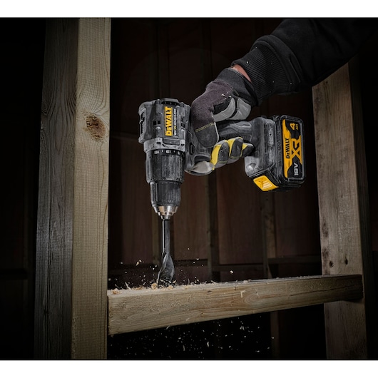 DEWALT cordless drill in use, drilling through wooden beams, close-up of tool and gloved hand.