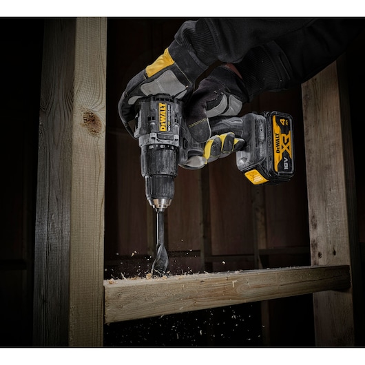 DEWALT cordless drill in use on wood, with worker wearing protective gloves.