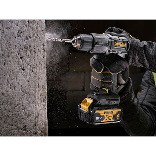 A DEWALT cordless drill with 18V XR battery drilling into concrete, operator wearing protective gloves.