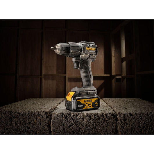 DEWALT 18V XR cordless drill stands on two concrete blocks in a dimly lit unfinished room.