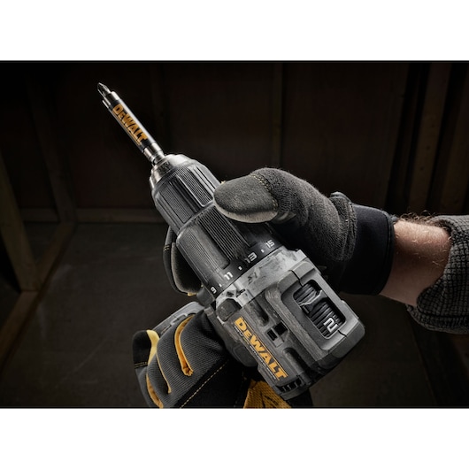 A gloved hand holding a DEWALT cordless drill with adjustable settings in a workshop.