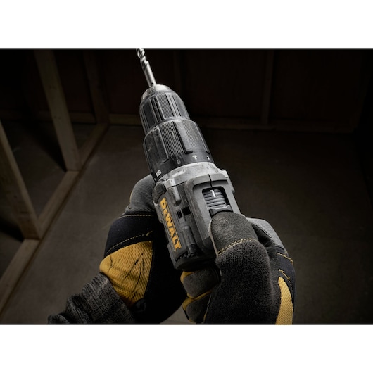Gloved hands hold a DEWALT cordless drill with a drill bit attached, shown in a construction setting.