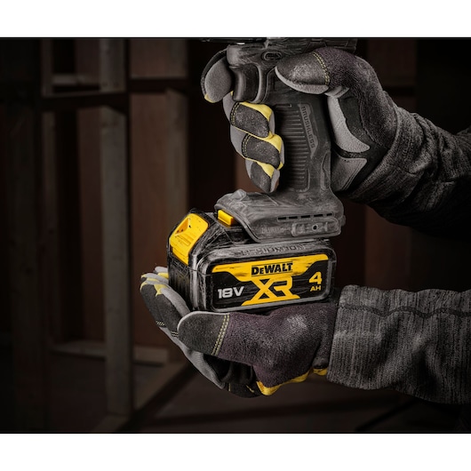 Gloved hands holding a DEWALT 18V XR 4Ah battery attached to a power tool, with a dark construction background.