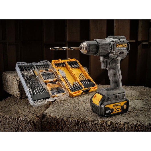 A DEWALT cordless drill with an attached drill bit is displayed on a concrete surface. Next to it are two open cases containing various drill bits and accessories, organized in yellow and transparent plastic cases.