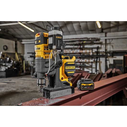 DEWALT magnetic drill and battery on steel beam in an industrial workshop.