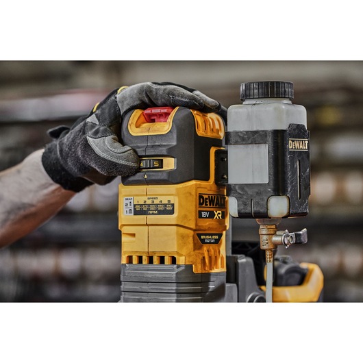 Gloved hand adjusts DEWALT 18V XR brushless motor tool with attached container in workshop.