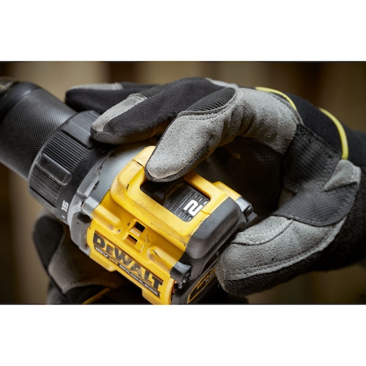 Close-up of a gloved hand adjusting the settings on a yellow DEWALT power drill, showing the selector switch and brand label.