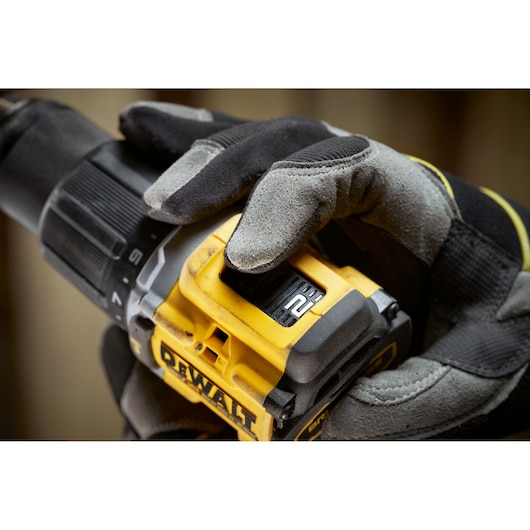 Close-up of a gloved hand adjusting the speed setting on a yellow DEWALT cordless drill.