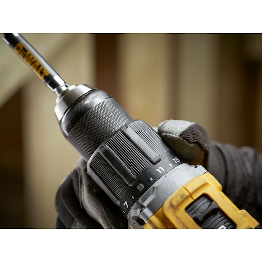 Close-up of a DEWALT cordless drill being held by a gloved hand, with focus on the adjustable torque settings and drill bit.