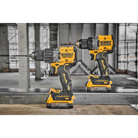 Two DEWALT cordless power drills, model DCD800E1T, are shown standing upright on a metal surface in a construction environment. Both drills feature yellow and black casing and are equipped with 18V POWERSTACK batteries.