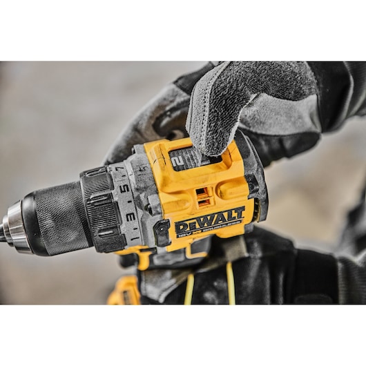 A close-up of a gloved hand adjusting the settings on a DEWALT cordless power drill.
