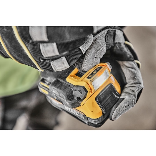 Close-up of a gloved hand holding a DEWALT power tool, focusing on the control panel and built-in LED light.