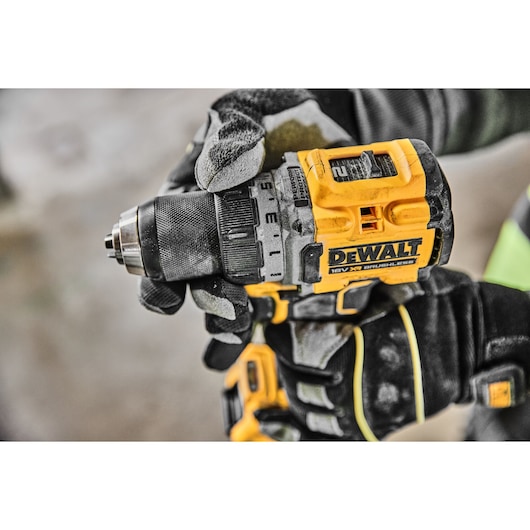 Close-up of a gloved hand holding and using a yellow and black DEWALT 18V XR brushless cordless drill.