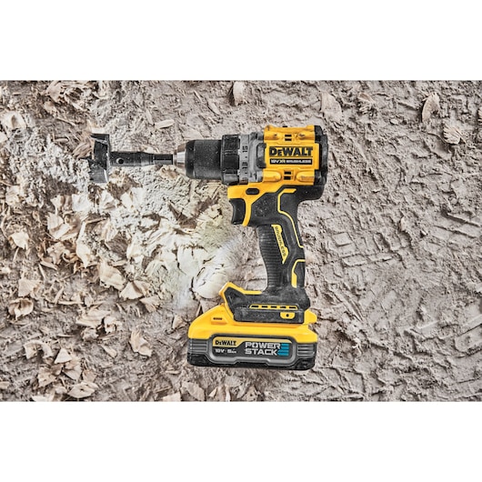 DEWALT cordless drill with PowerStack battery drilling into wood, surrounded by wood shavings.