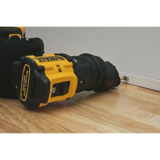A close-up of a DEWALT DCD803P2T cordless drill being used to drive a screw into a piece of white furniture, placed on a wooden floor.