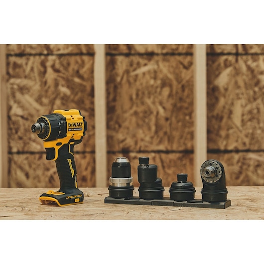 A yellow and black cordless power drill with multiple interchangeable attachments displayed on a wooden surface, set against a background of unfinished wooden walls.