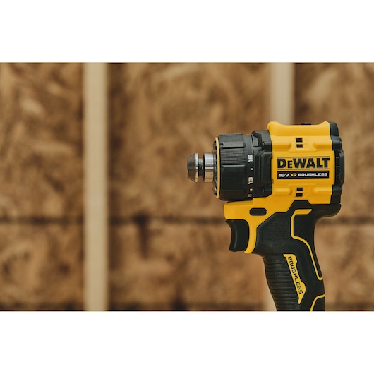 A DEWALT 18V XR brushless cordless drill shown against a blurred wooden background. The drill is yellow and black with the DEWALT logo clearly visible.
