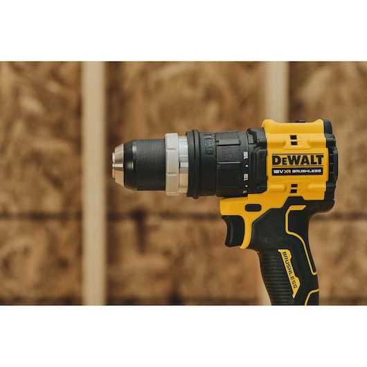 Close-up of a yellow and black DEWALT 18V XR brushless cordless drill held upright in front of a blurred wooden background.