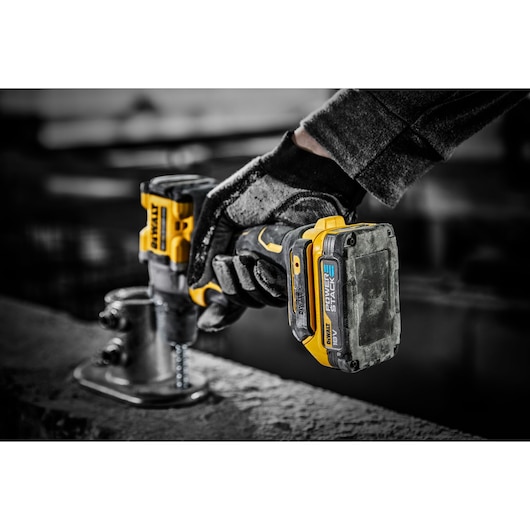 A close-up of a gloved hand using a yellow and black DEWALT 18V cordless drill to fasten a screw into a metal bracket on a