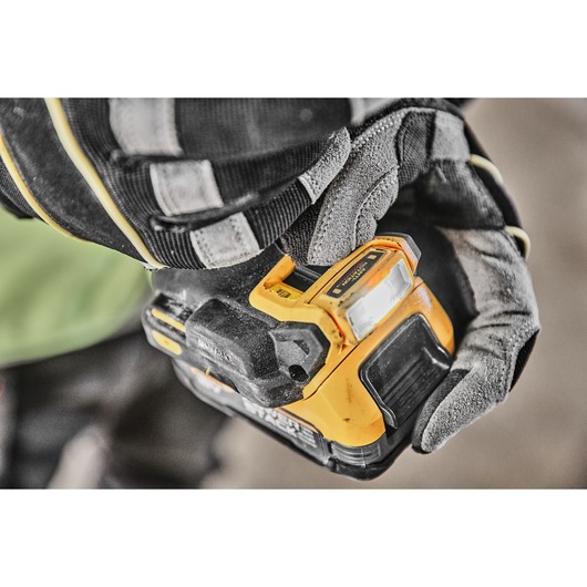 A close-up of a gloved hand operating a yellow and black DEWALT cordless power tool.