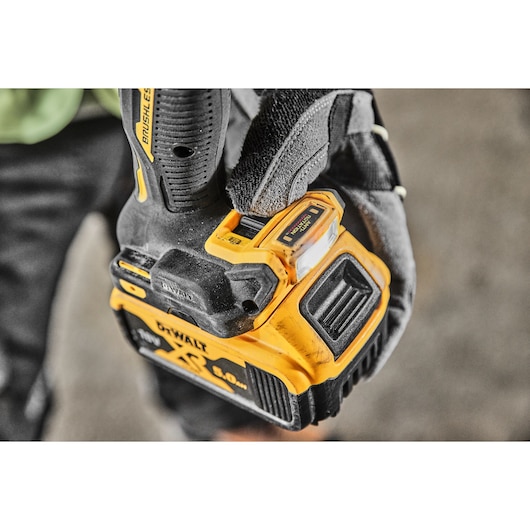 Close-up of a gloved hand holding a DEWALT cordless power drill with a 5.0Ah XR battery attached.