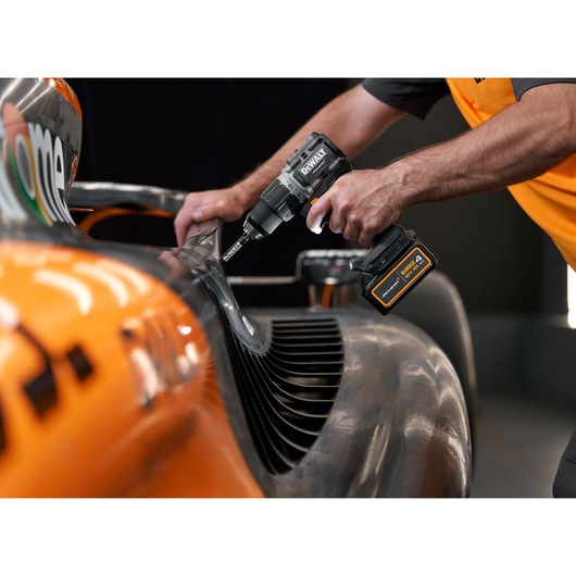 A person using a DEWALT cordless power drill to work on the body of an orange and black racing car.