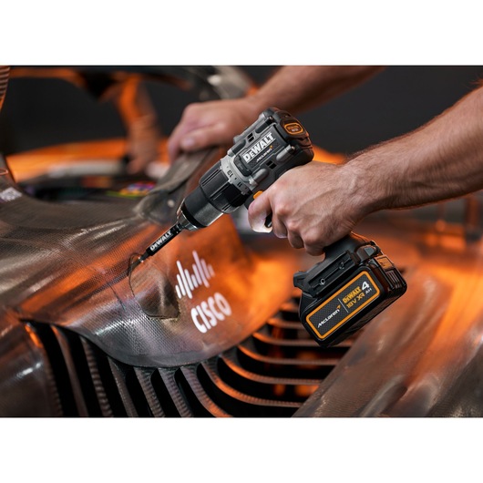 A person using a DEWALT cordless power drill on a carbon fiber surface, likely part of a vehicle, with the Cisco logo visible. The scene is well-lit and focused on the tool and area being drilled.