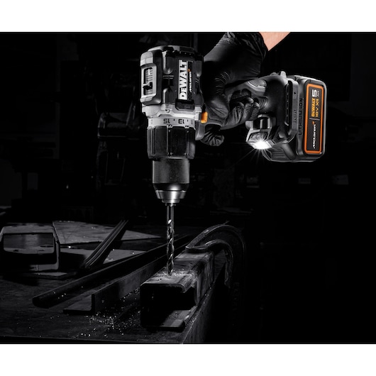 DEWALT cordless drill in use on metal, held by a gloved hand with LED light illuminating the work area.