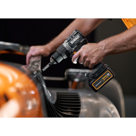 DEWALT cordless drill in use on a metal surface, held by a person working on machinery.