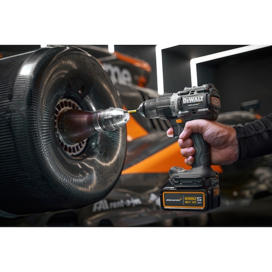 Hand using DEWALT cordless drill on a race car wheel. McLaren branding is visible on the tool.