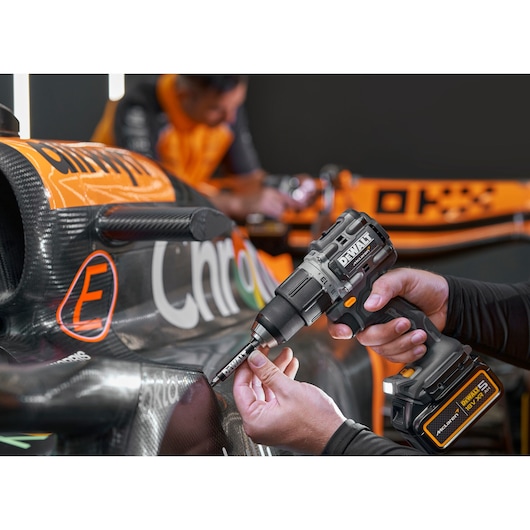 DEWALT cordless drill being used on a race car's carbon fiber body, with hands holding the tool.