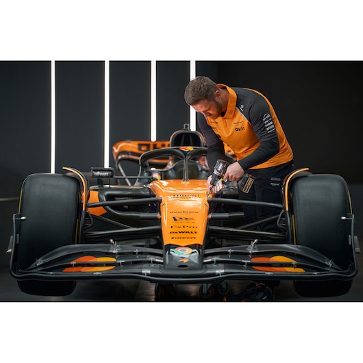 Person using a DEWALT tool on an orange race car in a garage, facing forward.