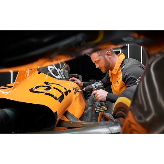 Person uses DEWALT drill on an orange race car viewed close-up, with blurred face and team uniform visible.